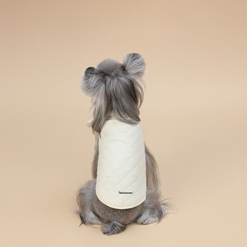 Dog wearing a white quilted jacket on a beige background