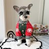 Dog wearing a red and green jacket with buttons on a white rug.