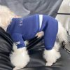 White dog wearing a blue hoodie with 'Essential' branding on a black surface.