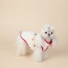 Small white dog wearing a red and white outfit with a bow on a beige background