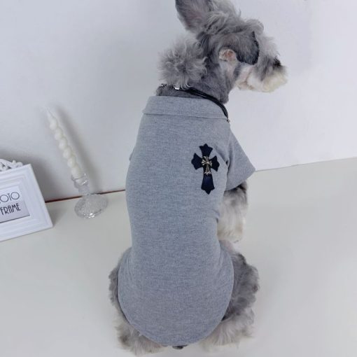 Dog wearing a gray chrome heart polo with a black cross design on a white surface.