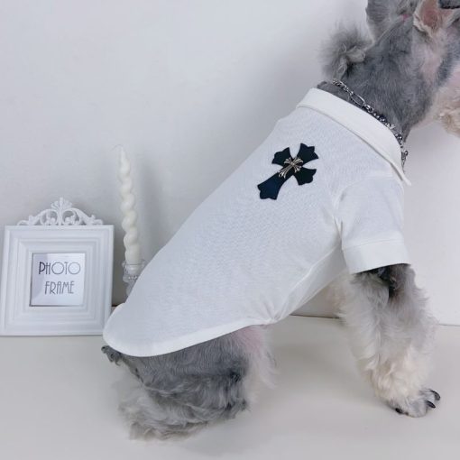 Dog wearing a white chrome heart polo shirt with a black emblem on a light gray background